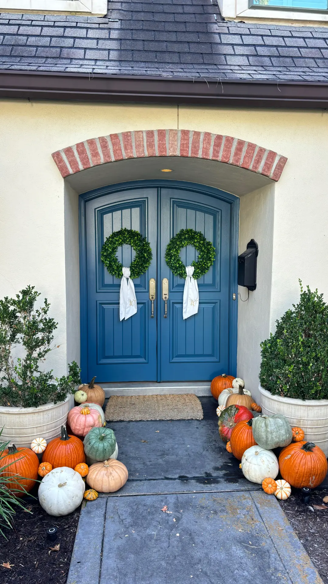 Blue arched double doors framed by heirloom pumpkins and boxwood wreaths, styled by West Pumpkin Bros
