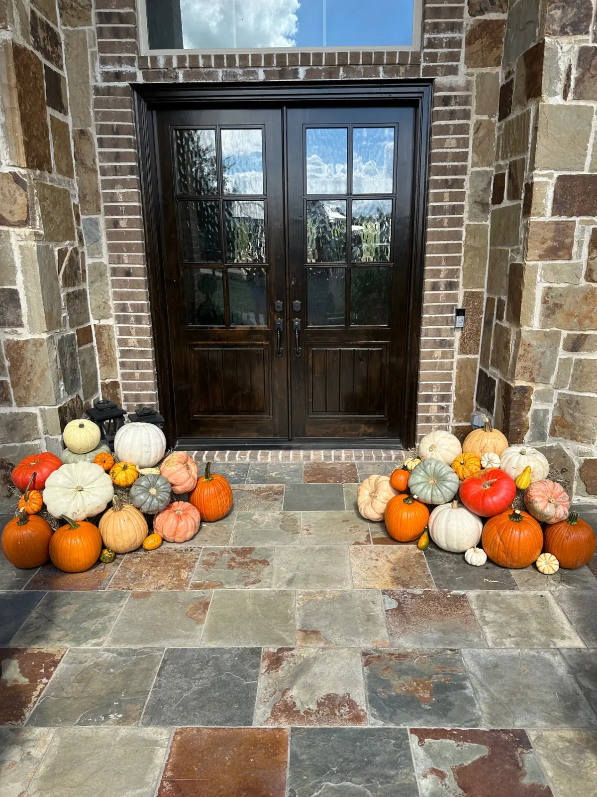 Stone entry with heirloom pumpkins flanking dark double doors, styled by West Pumpkin Bros