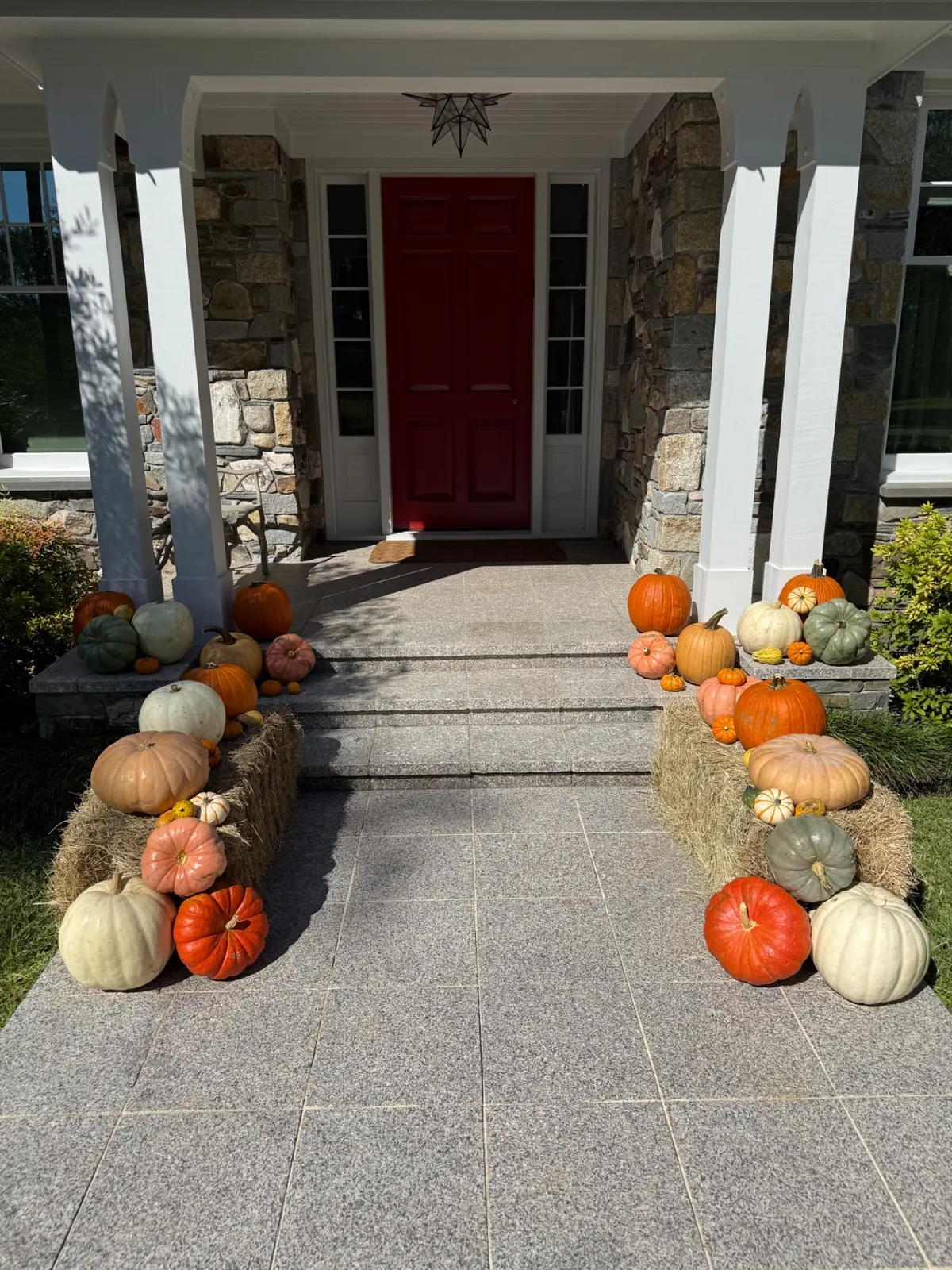 Stone walkway lined with hay bales and heirloom pumpkins leading to a red front door, styled by West Pumpkin Bros