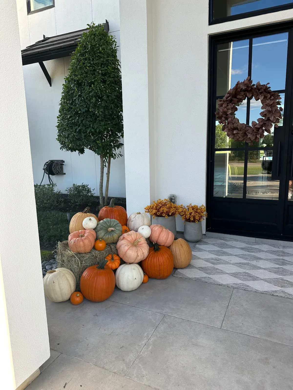 Pumpkins layered on hay bales beside a black steel front door, styled by West Pumpkin Bros